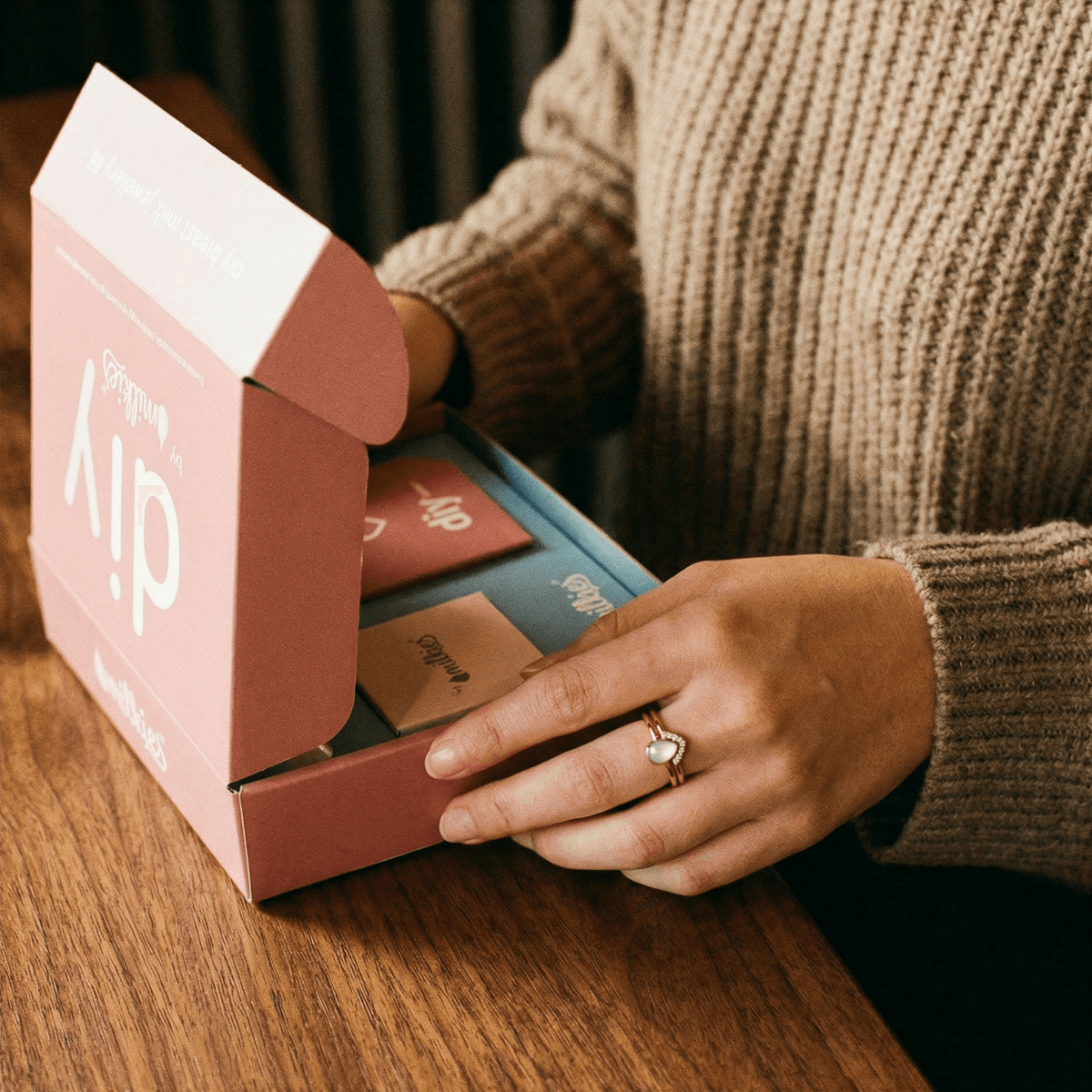 Kit DIY by MILKIES ouvert sur une table, avec une main portant une bague lactée, idéal pour créer chez soi des bagues allaitement et préserver un souvenir intime en toute confidentialité.