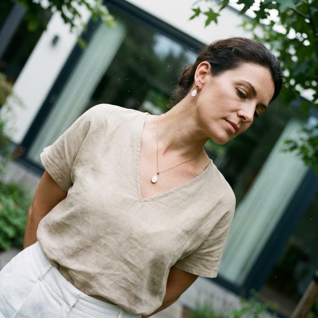 Femme dans un jardin devant une baie vitrée portant un collier et des boucles d’oreilles en forme de goutte, inspirés des bijoux lait maternel diy.