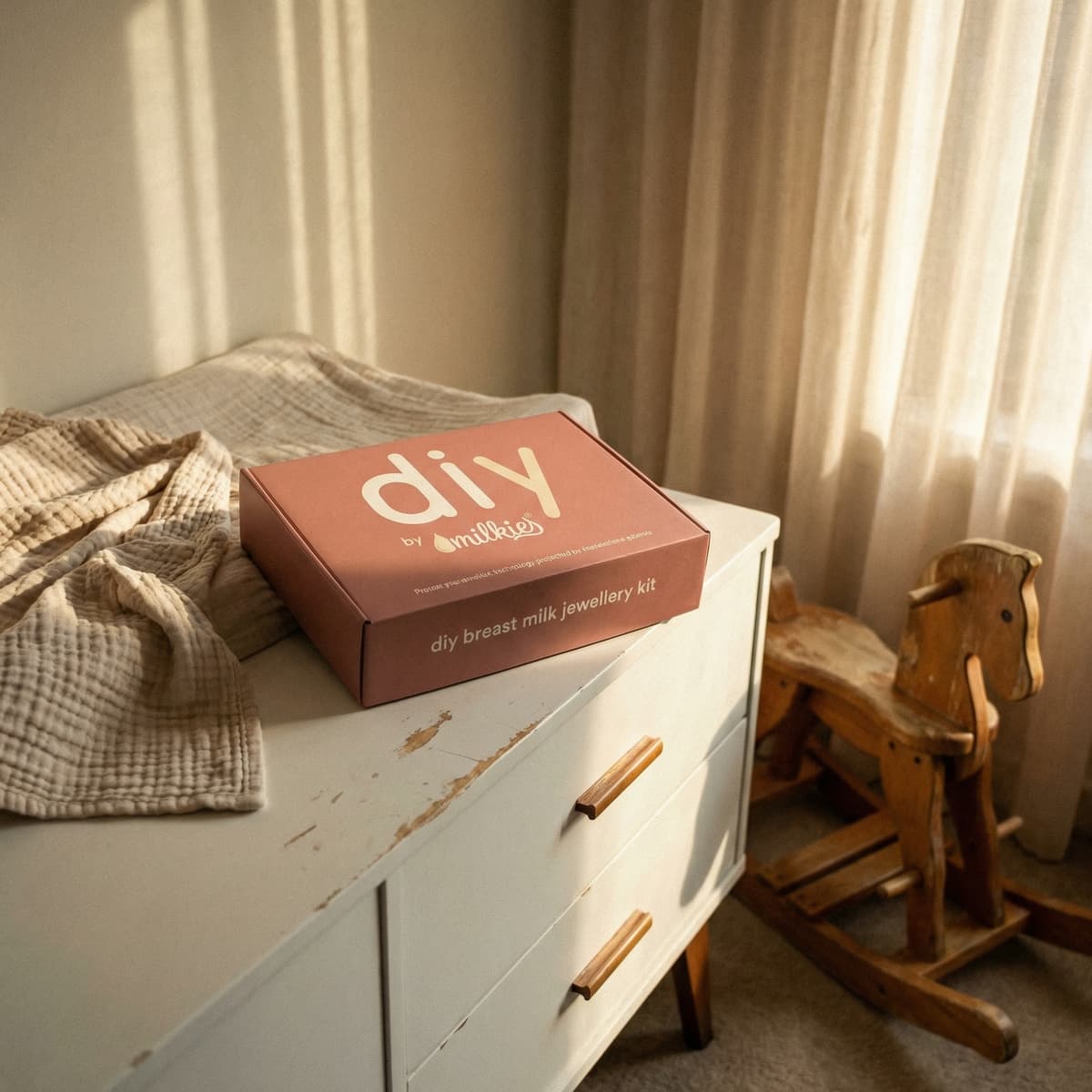 Boîte du kit DIY by MILKIES pour créer un bijou au lait maternel, posée sur une commode dans une chambre de bébé, idée de cadeau femme enceinte