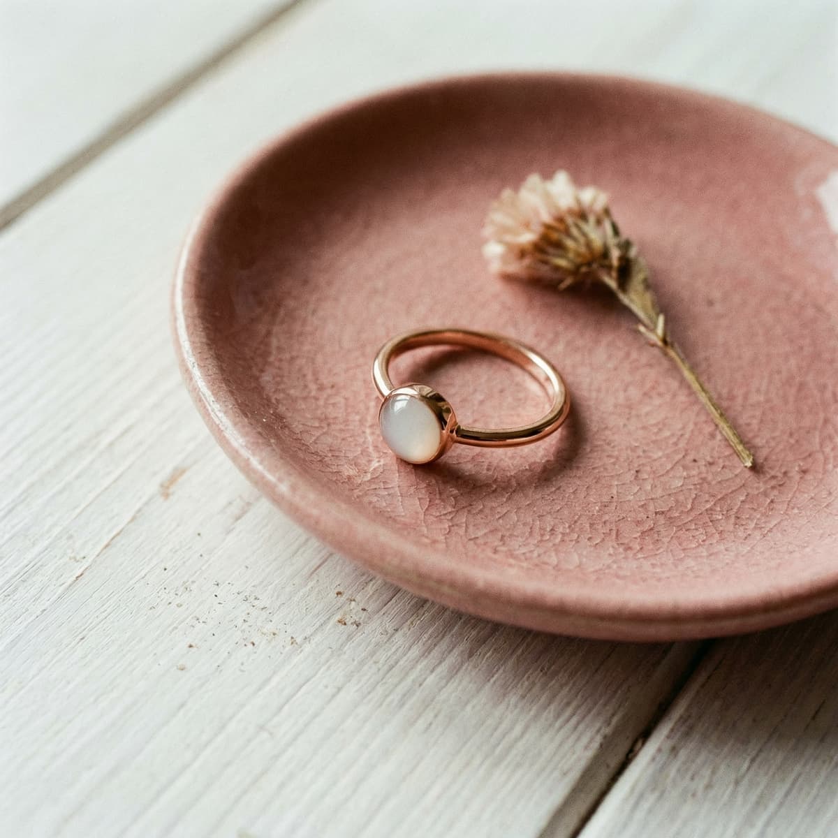 Sur une assiette en céramique rose, une bague en or avec pierre lactée blanche, visuel d’inspiration pour un kit bague lait maternel et un souvenir d’allaitement.