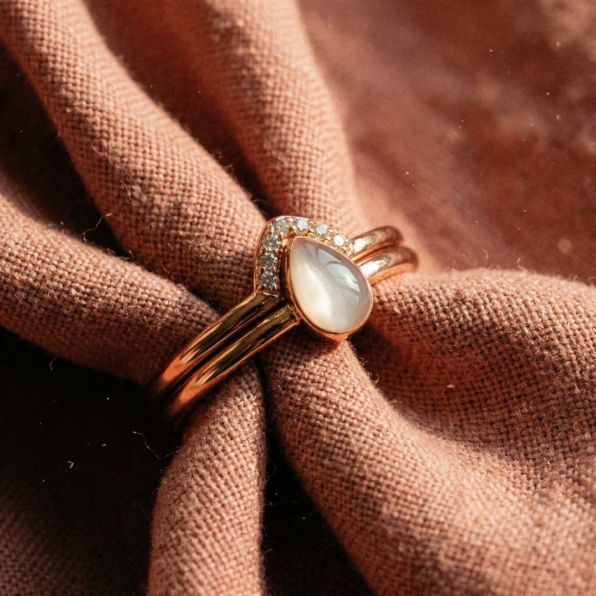 Bague couleur or rose avec pierre opalescente en forme de goutte et petits cristaux, posée sur un tissu noué, parfaite pour un kit diy bague lait maternel DIY by MILKIES.
