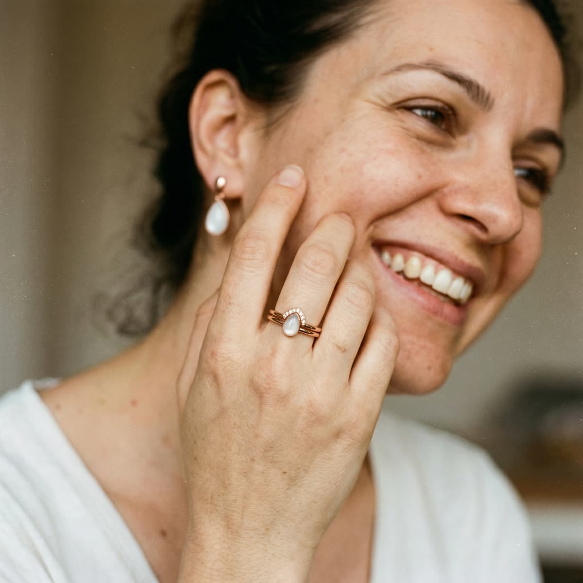 Jeune maman souriante portant une bague et une boucle d’oreille avec pierre blanche, illustrant pourquoi choisir un kit diy bague lait maternel pour créer chez soi un bijou souvenir intime et durable.