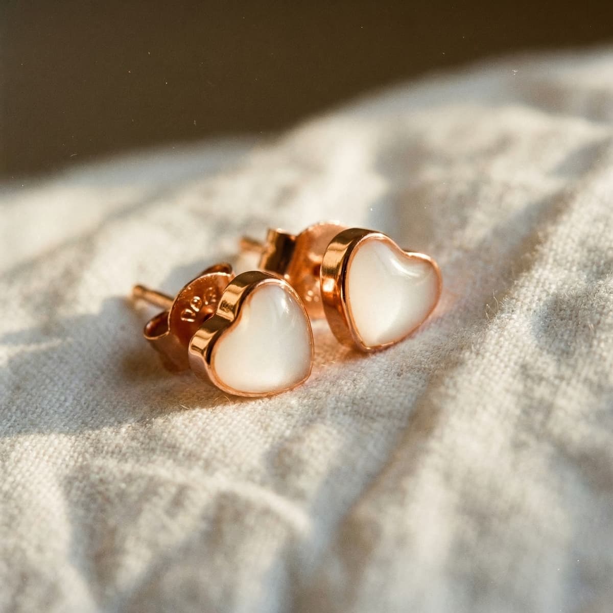 Gros plan de boucles d’oreilles en forme de cœur avec résine blanc nacré et cadre rose doré, un modèle de boucles d’oreilles allaitement diy posé sur un tissu clair à la lumière douce.