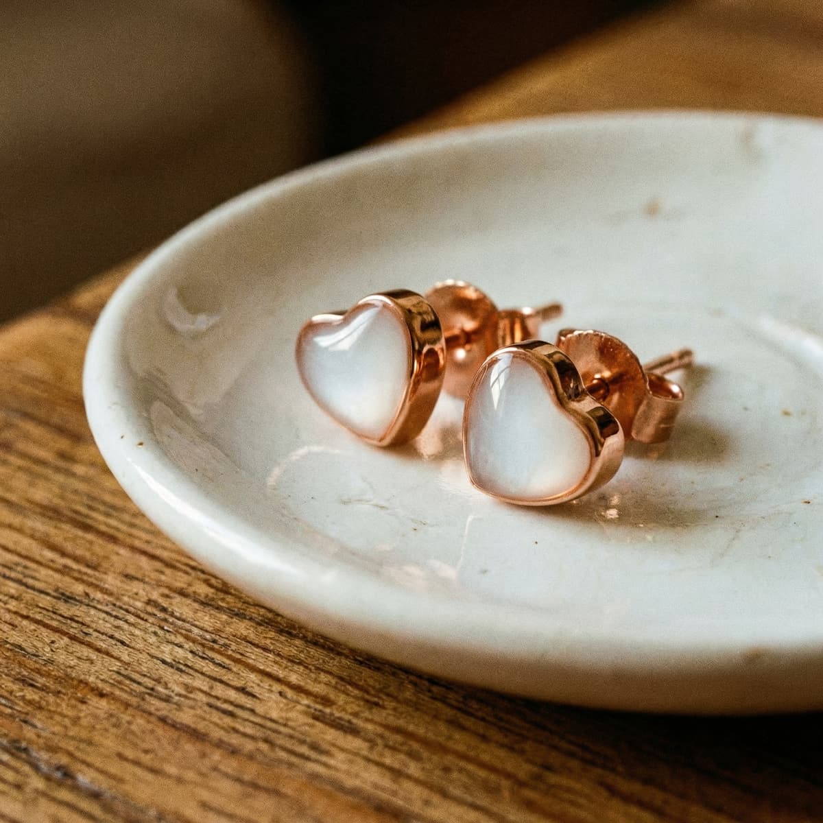 Boucles d’oreilles en forme de cœur rose gold, serties de résine blanche effet lait maternel, idéales comme boucles d’oreilles lait maternel à faire soi-même, présentées sur une coupelle en céramique.
