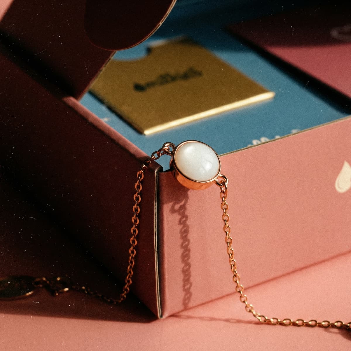 Chaîne dorée avec cabochon rond blanc nacré, bracelet souvenir lait maternel posé sur une boîte rose du kit DIY by MILKIES.