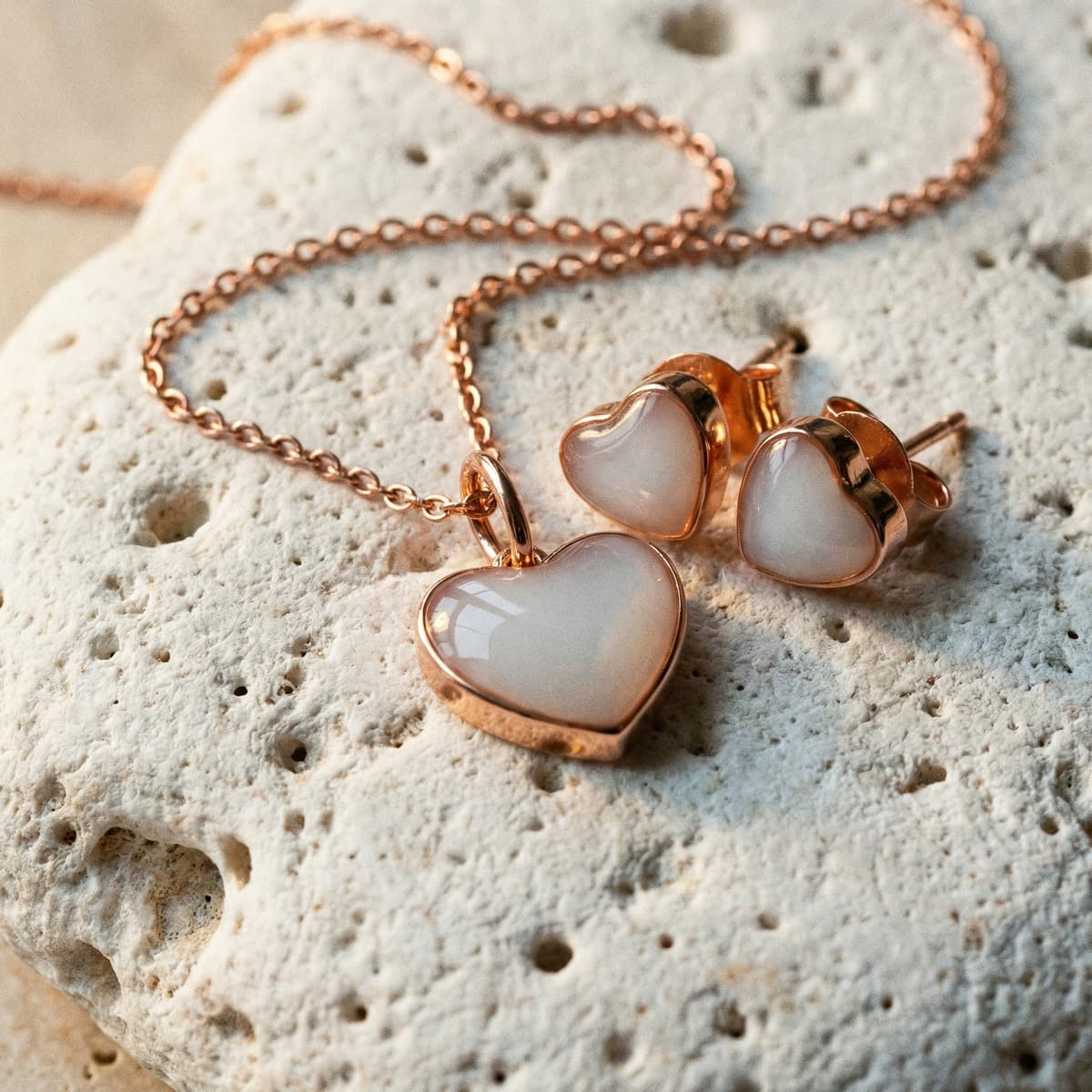 Bijou souvenir en forme de cœur, collier et boucles d’oreilles dorés rose avec pierre blanche nacrée sur fond minéral, idée de cadeau naissance original maman.