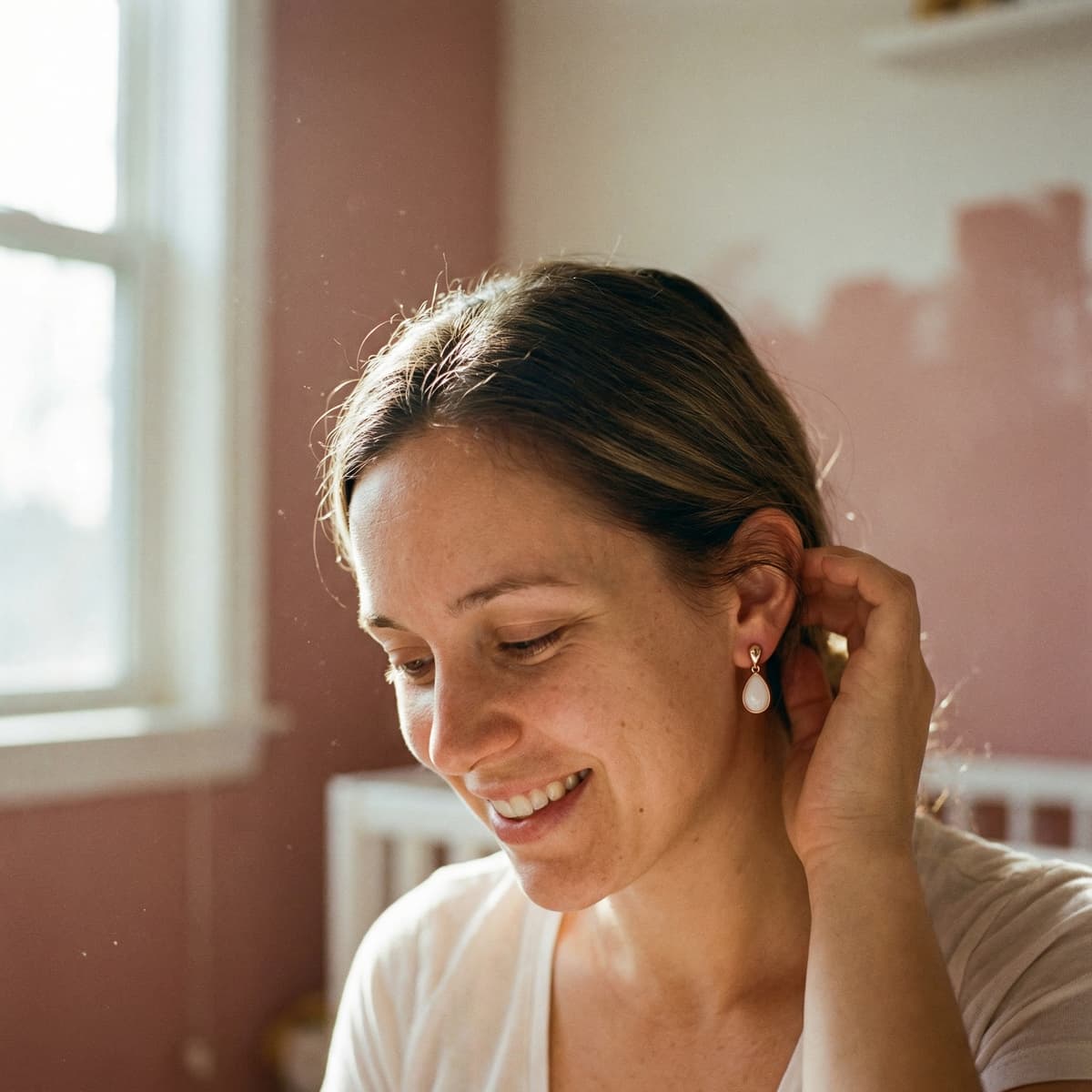 Jeune maman souriante portant une boucle d’oreille goutte blanche sertie or, illustrant pourquoi faire des boucles d'oreilles lait maternel avec un kit DIY est une idée simple et précieuse pour créer un souvenir intime à la maison.