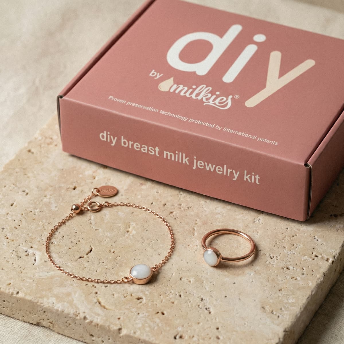 Coffret DIY by MILKIES dans une boîte rose « DIY breast milk jewelry kit » avec bracelet et bague dorés sertis d’une pierre blanche, pour faire un bracelet avec son lait à la maison.