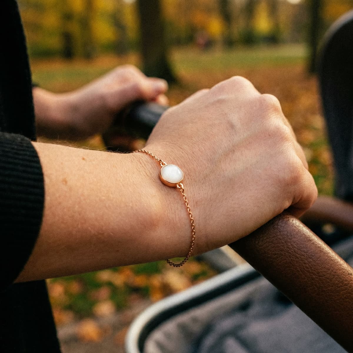 Bracelet en chaîne dorée porté au poignet d’une maman, avec pendentif rond blanc réalisé avec un kit bracelet lait maternel lors d’une promenade en plein air.