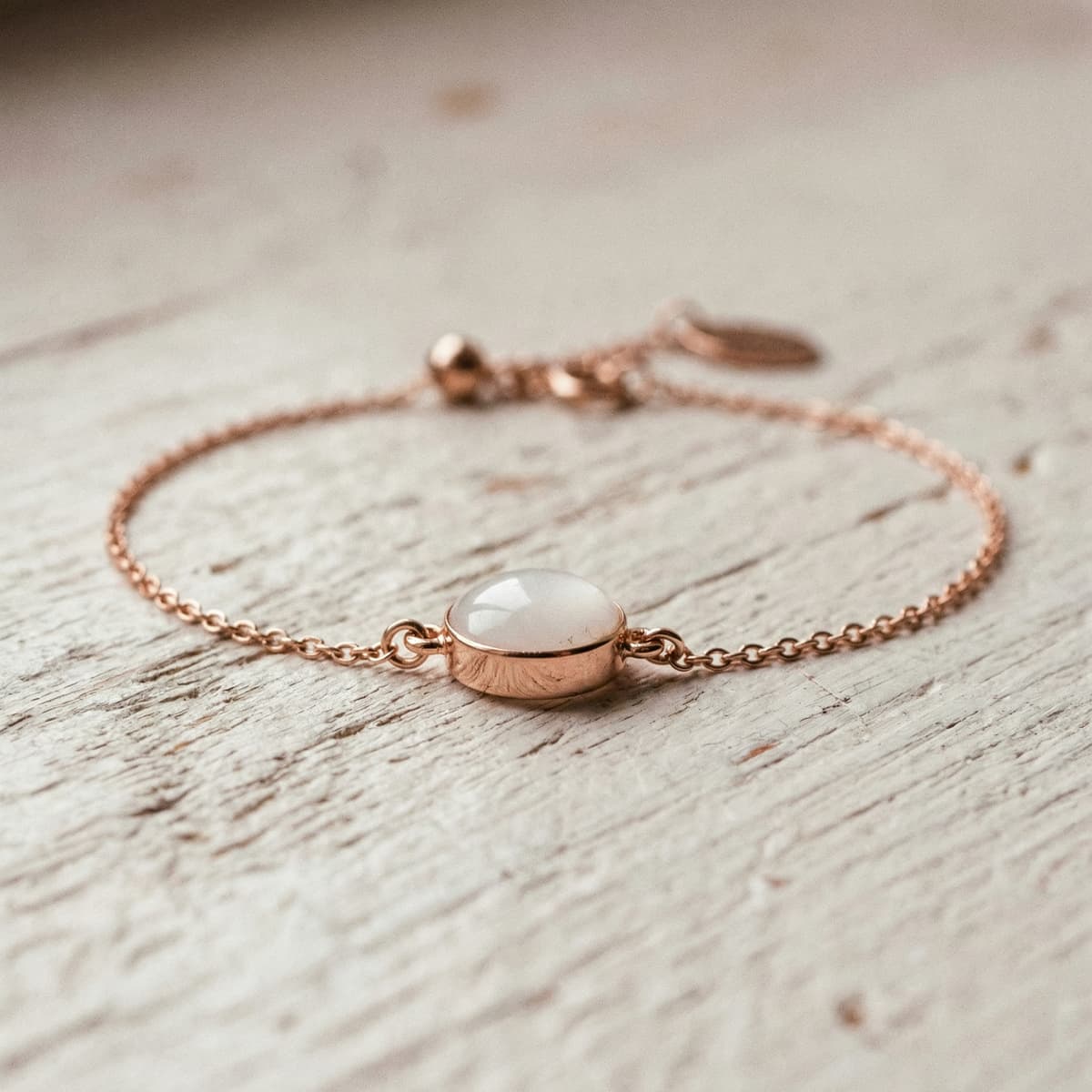 Bracelet chaîne en or rose avec une perle lait maternel en cabochon blanc laiteux, présenté en gros plan sur une surface en bois clair.